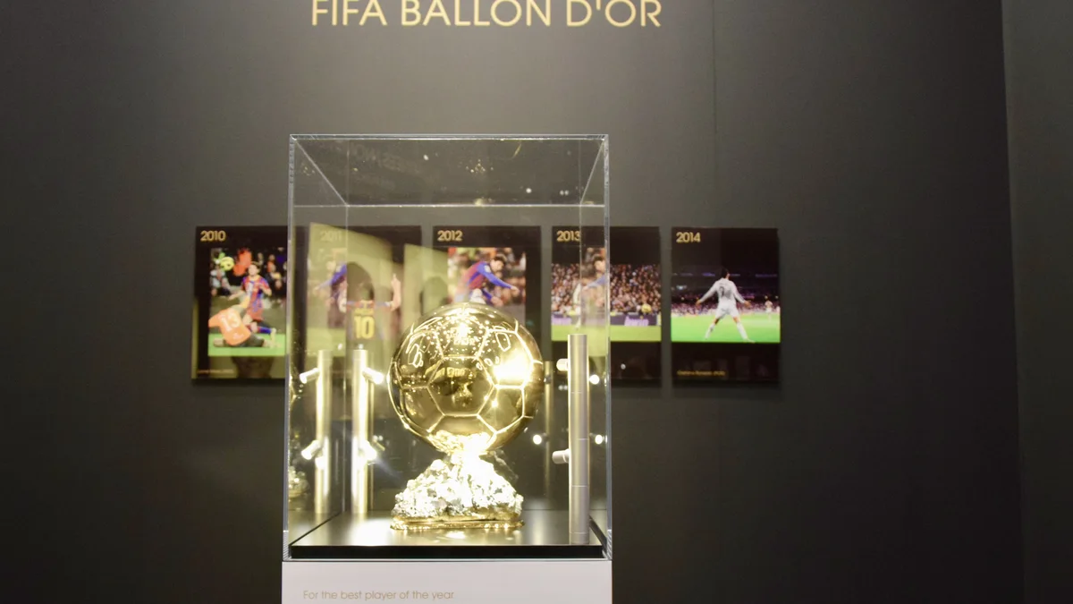 Le trophée du Ballon d'Or exposé sous vitrine, avec les photos des lauréats en arrière-plan