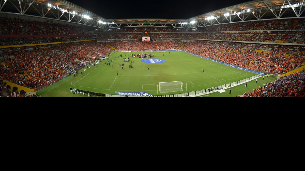 Panoramic view of a packed Suncorp Stadium in Brisbane at night, orange stands lit up, during a match