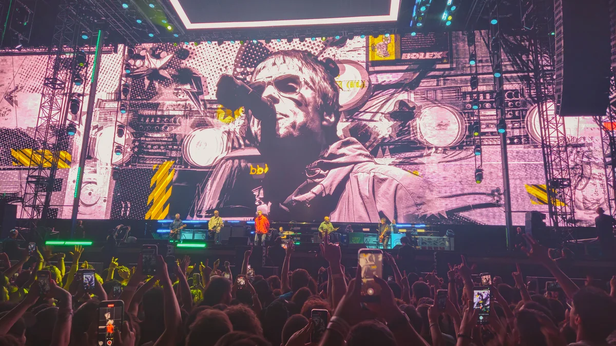 Liam Gallagher projeté sur un grand écran de scène, foule compacte au premier plan, lors d'un concert d'Oasis en 2025