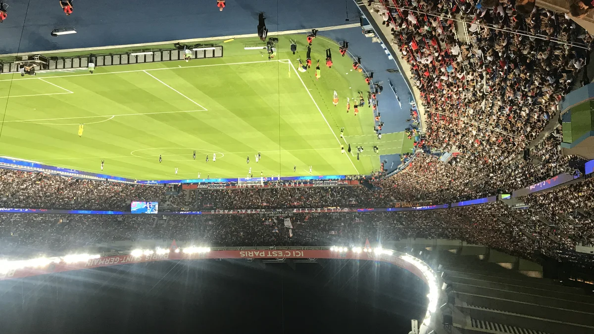 Le Parc des Princes plein en nocturne, tribunes illuminées et banderole « Ici c'est Paris », pendant un match du PSG