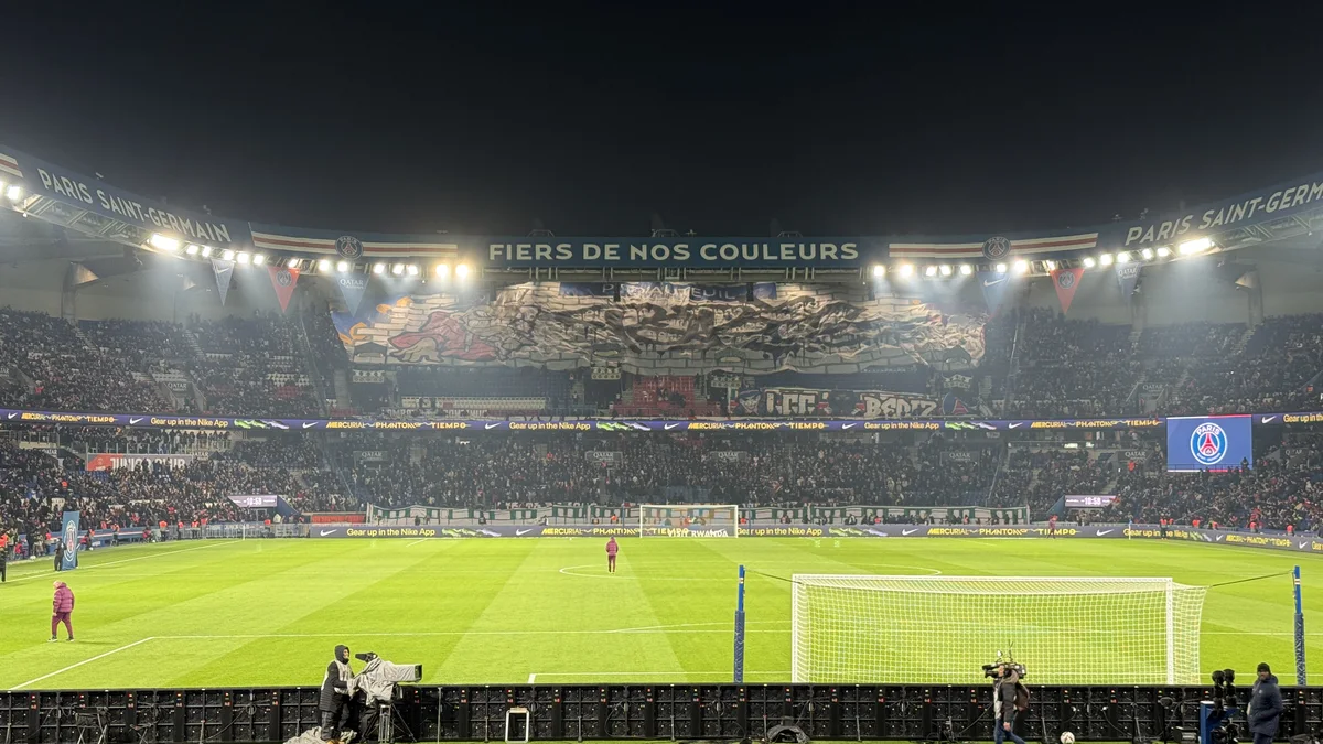 Un grand stade de football plein en nocturne, tribunes illuminées, pendant un match de haut niveau